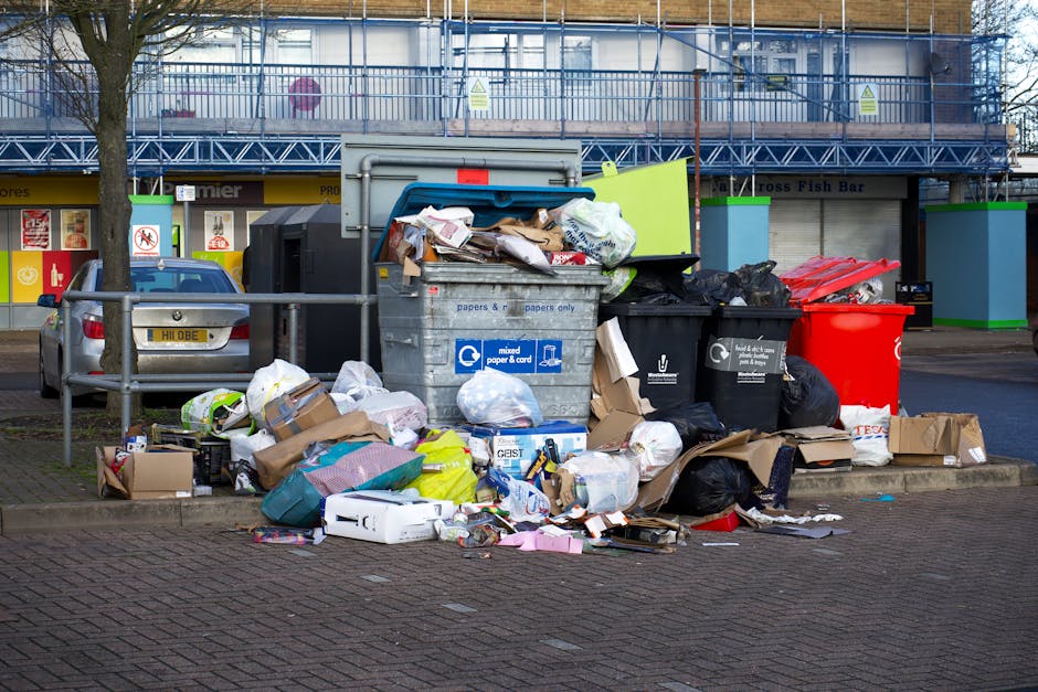 A close-up view of a large pile of crushed and crumpled aluminium drink cans and food packaging materials, primarily in silver, gold, red, blue, and black colors, with various brand labels and barcode